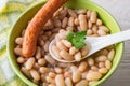White backed beans, thin sausage and ceramic spoon in a green bowl. Bean is source of vegetable protein and ingredient for
