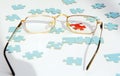 On a white background blue puzzles. A red puzzle is visible through the lens of the glasses.