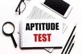 On a white background glasses a magnifier pencils a smartphone and a notebook with the text APTITUDE TEST