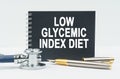 On a white background lies a stethoscope, a pen and a black notebook with the inscription - LOW GLYCEMIC INDEX DIET Royalty Free Stock Photo