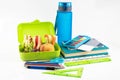 On a white background, a lunch box with a sandwich, vegetables and fruits, a bottle of water and school supplies Royalty Free Stock Photo