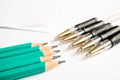 On a white background are simple graphite pencils and pens in front of pencils, paper sheets in the background Royalty Free Stock Photo