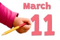 White background with spring red date, business and holiday concept. The child`s hand writes March 11 with colored pencil
