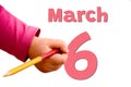 White background with spring red date, business and holiday concept. The child`s hand writes March 6 with colored pencil