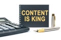 On a white background, there is a calculator, a pen and a black notebook with the inscription - CONTENT IS KING