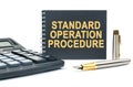 On a white background, there is a calculator, a pen and a black notebook with the inscription - STANDARD OPERATION