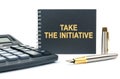 On a white background, there is a calculator, a pen and a black notebook with the inscription - TAKE THE INITIATIVE