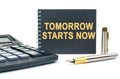 On a white background, there is a calculator, a pen and a black notebook with the inscription - TOMORROW STARTS NOW