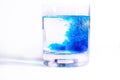 On a white background transparent glasses with water, in each drip blue paint. Ink blurs in the water, form beautiful patterns.