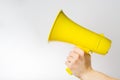 On a white background, a yellow megaphone in a female hand. Symbol of fakes, misinformation. Elections, journalism, yellow press,