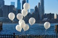 White balloons tied to a railing in Brooklyn Bridge Park. Behind is the East River and the skyline of Lower Manhattan