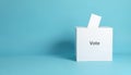 White ballot box with black text label, gray vote button. Solid blue background emphasizes form, function of vote container. Royalty Free Stock Photo