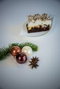 On white base a piece of cake on a white plate and christmas decoration