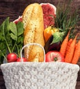 White basket full of groceries and vegetables on wood background