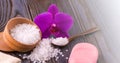 White bath salt in a wooden bowl with a spoon, soap, burlap and orchid on wooden table on sunlight Royalty Free Stock Photo