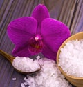 White bath salt in a wooden cup with a spoon on a wooden table with an orchid. Royalty Free Stock Photo