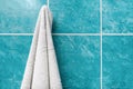White bath towel hanging on the hook in an ordinary home bathroom with blue tiles with copy space, shower and every day