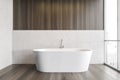 White bathtub on wooden floor in bathroom near window, white wooden design Royalty Free Stock Photo