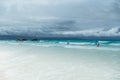 White Beach of Boracay and people swim at turquoise azure Sea on a cloudy day near Grotto Willy`s Rock upon which stands