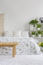 White bedroom interior with fresh plants on rack, floral sheets on double bed, carpet on the floor Royalty Free Stock Photo