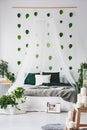 White bedroom interior with king size canopy bed with emerald pillows and grey blanket, urban jungle and green leafs on the wall