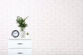 White bedside table with clock and green plants on brick wall ba Royalty Free Stock Photo