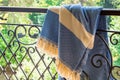 A white beige and blue Turkish peshtemal / towel on a wrought iron railings with blurry nature in the background. Royalty Free Stock Photo