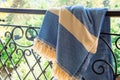 A white beige and blue Turkish peshtemal / towel on a wrought iron railings with blurry nature in the background. Royalty Free Stock Photo