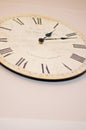 White and beige wooden wall clock with Roman numerals and black metallic hands, needles or pointers on a white wall. Old vintage