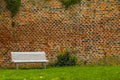 White bench standing in front of an old brick wall in a city park.