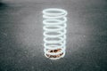White big, giant spring on a black background. White very large and thick metal spring sticks out of the ground, attached to the Royalty Free Stock Photo