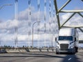 White big rig bonnet semi truck transporting cargo in dry van semi trailer running on the arched bridge with powerful rope bridge