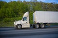 Profile of white big rig day cab semi truck with roof spoiler transporting commercial cargo in dry van semi trailer going on the