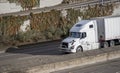 White big rig industrial semi truck carry goods in dry van semi trailer driving on the highway with multilevel road entrance and Royalty Free Stock Photo