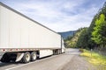 White big rig long haul industrial semi truck transporting goods in dry van semi trailer with skirt driving on the winding road Royalty Free Stock Photo