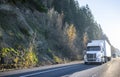 White big rig semi truck with dry van semi trailer driving in front of another semi trucks and cars traffic on wide highway Royalty Free Stock Photo