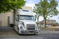 White big rig semi truck with grille guard and refrigerator semi trailer unloading cargo standing at warehouse dock gate at Royalty Free Stock Photo