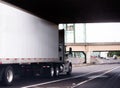 White big rig semi truck with day cab and dry van trailer running on the road under bridge Royalty Free Stock Photo