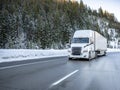 White big rig semi truck tractor with dry van semi trailer climbing uphill on the dangerous slippery winter road with snow and ice Royalty Free Stock Photo