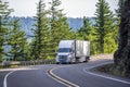 White big rig semi truck transporting goods in refrigerated semi trailer turning on the mountain road with rock wall Royalty Free Stock Photo