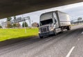 White big rig semi truck transporting industrial cargo on dry van semi trailer running under the bridge across the wide highway