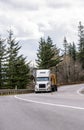 White big rig semi truck transporting lumber wood on flat bed semi trailer driving on winding mountain road