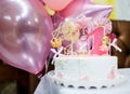 White birthday cake with pink candles as decorations on the table on pink air ballons background. Celebration, festive background,
