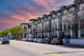 A white and black apartment building with parked cars on the street in front with lush green trees and blue sky Royalty Free Stock Photo