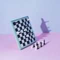White and black chess board and pieces defy gravity on pink and grey background. Minimal concept