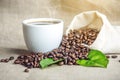 White black espresso Cup with a pile of coffee beans and green leaves in bag on white linen background Royalty Free Stock Photo