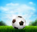 White and black soccer ball on the green glade with grass. Background with blue sky, sunshine and sport equipment for