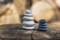 White black stone cairns, poise light pebbles on wood stump in front of brown natural background, zen like, harmony and balance Royalty Free Stock Photo