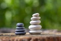 White black stone cairns, poise light pebbles on wood stump in front of green natural background, zen like, harmony and balance Royalty Free Stock Photo