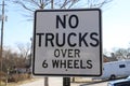 A white and black traffic sign that says `No Trucks Over 6 Wheels` with bare winter trees and blue sky in Douglasville Royalty Free Stock Photo